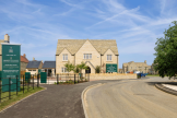 Brand new houses in Cotswold stone, on a sunny day. With signage at the entrance with open green space and plants