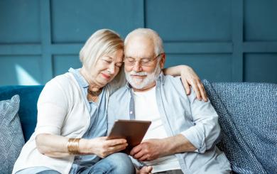 Lovely senior couple dressed casually using digital tablet while sitting together on the comfortable couch at home