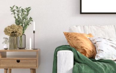 Minimalist living area, with modern white sofa positioned next to side table decorated with vases and candles.