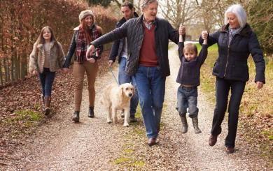 Happy grandparents, parents and children walking along a country road on an autumnal day, dressed up warm in coats and wellies with a golden retriever alongside them