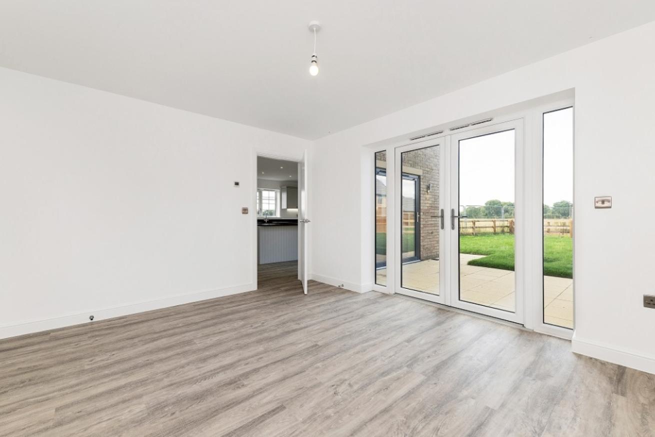 An empty room with patio doors out to the garden. Decorated all white with wooden flooring