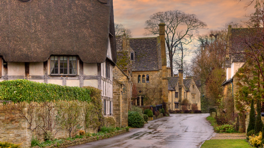 View of a quaint coutryside street in the cotswolds with thatched-rooved cottages and houses build with cotswold stone