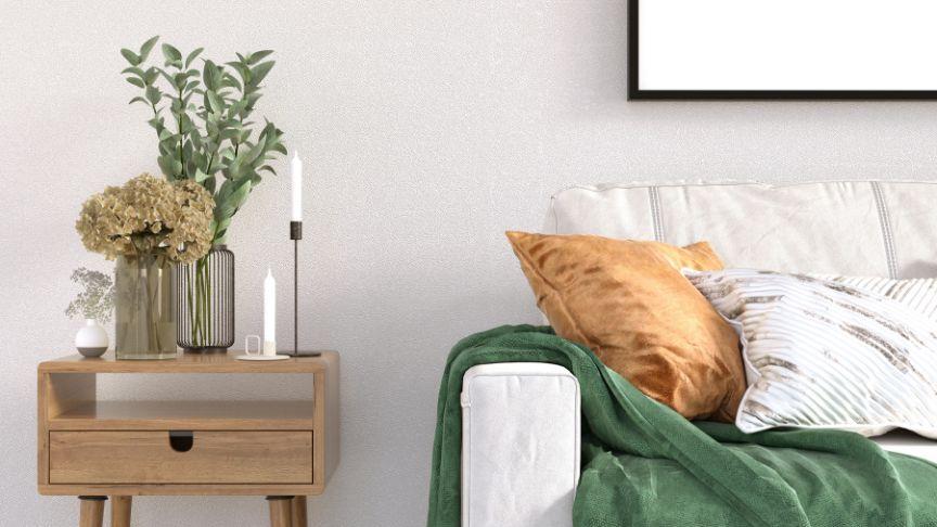 Minimalist living area, with modern white sofa positioned next to side table decorated with vases and candles.