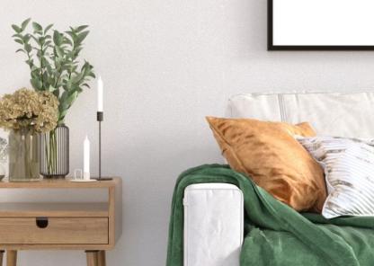 Minimalist living area, with modern white sofa positioned next to side table decorated with vases and candles.