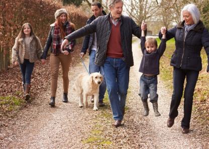 Happy grandparents, parents and children walking along a country road on an autumnal day, dressed up warm in coats and wellies with a golden retriever alongside them